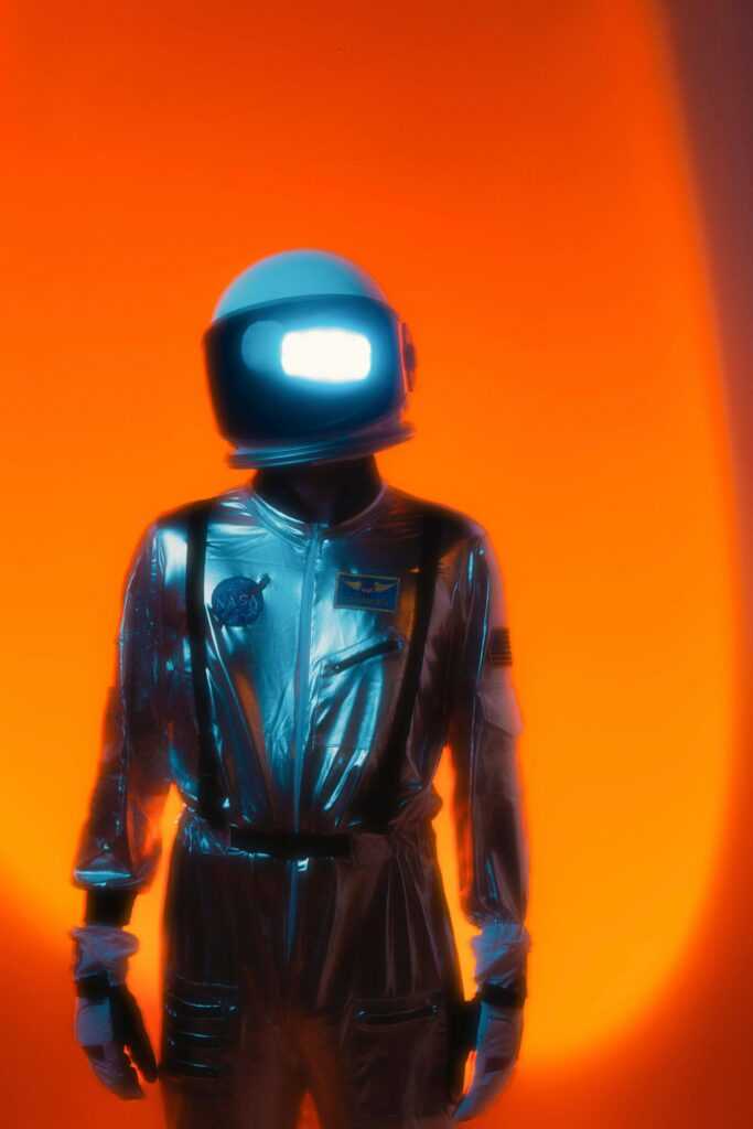 Explore space fashion with a futuristic astronaut helmet and reflective silver suit against a vivid orange backdrop.