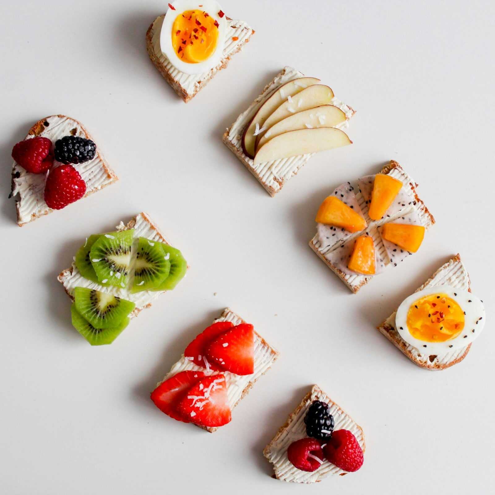 An artistic flat lay featuring a variety of fruit-topped cream cheese crackers, perfect for breakfast or brunch.