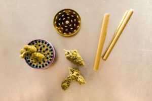 Flat lay of cannabis buds, grinder, and rolling papers on a table.
