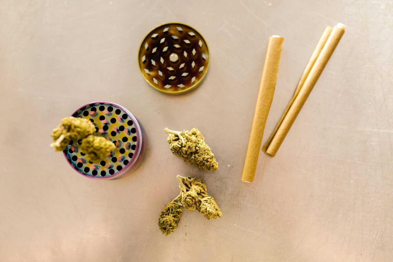 Flat lay of cannabis buds, grinder, and rolling papers on a table.